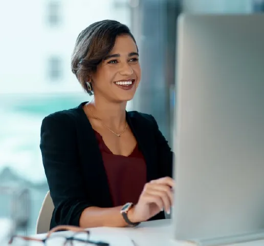 Smiling woman in business attire working at a computer in a bright office.