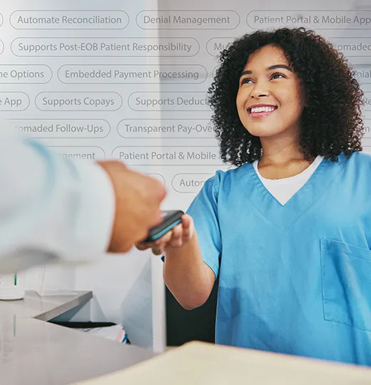 Smiling medical worker in blue scrubs accepting a payment card from a person at a counter.