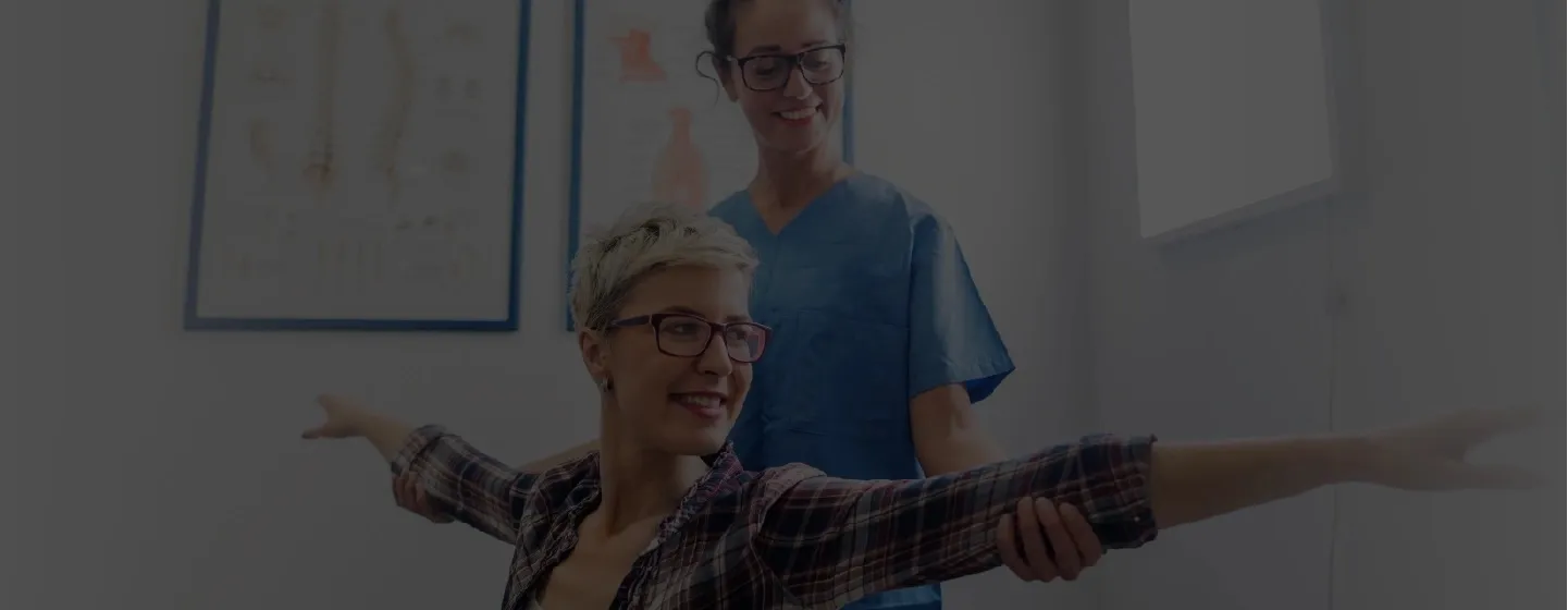 Physical therapist assists a smiling woman with outstretched arms during a rehab session.