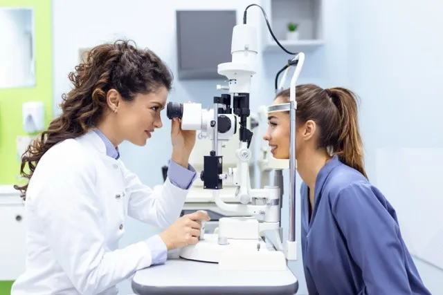 Eye doctor examining a female patient using a slit lamp in a bright clinical setting.