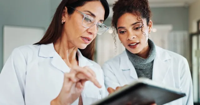 Two female doctors in white coats reviewing information on a digital tablet in a medical setting.