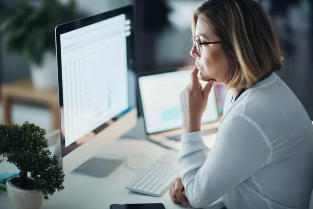 Woman in glasses looking at data on a desktop computer in a modern office setting.