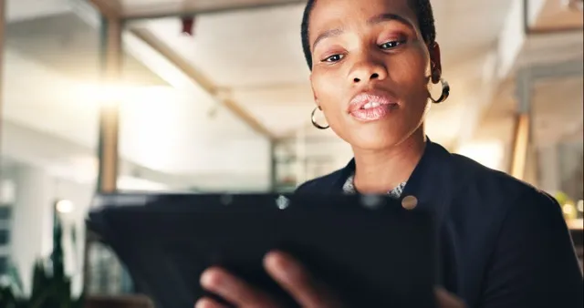 Focused woman in hoop earrings looking at a tablet in a bright indoor space.