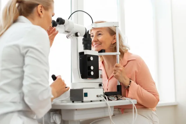 Woman undergoing an eye exam using a slit lamp with an optometrist in a bright clinic.