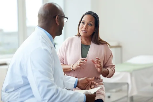 Woman in pink sweater talking with a male doctor in white coat in a bright medical office.