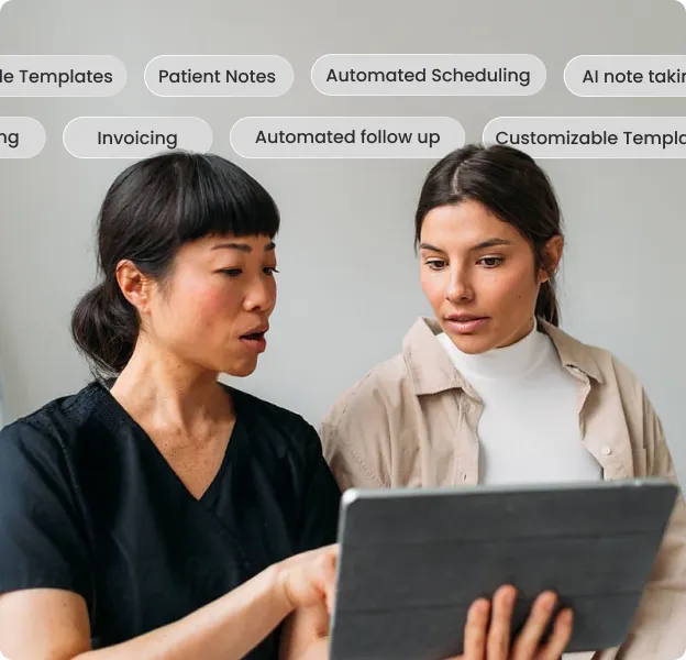 Two women looking at a tablet, one in black scrubs and the other in a beige jacket.