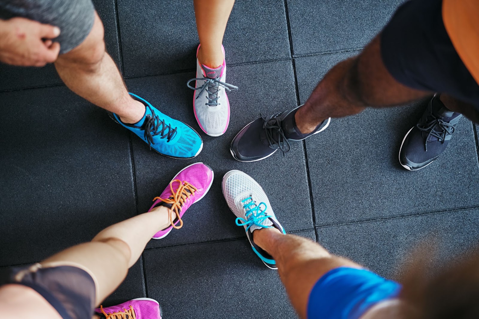 Group of people wearing colorful athletic shoes standing in a circle on a gym floor.