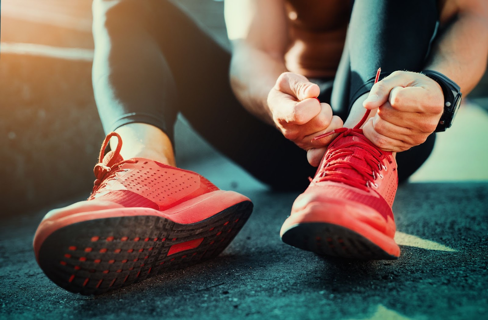 Person tying red running shoes on a track at sunset.