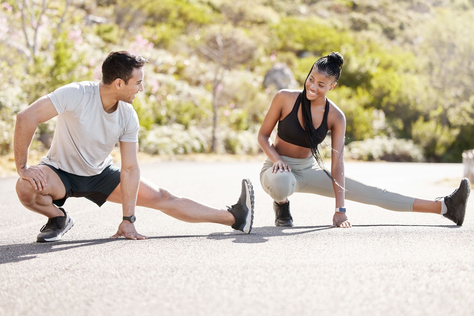 Two people stretching on a road with greenery in the background.