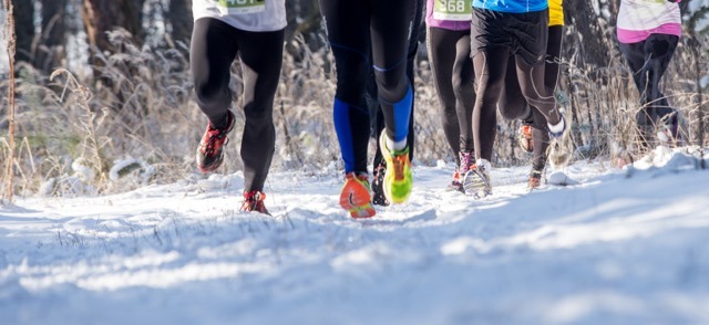A team of people in athletic wear running on a snow-covered path, highlighting their commitment to outdoor exercise in winter.