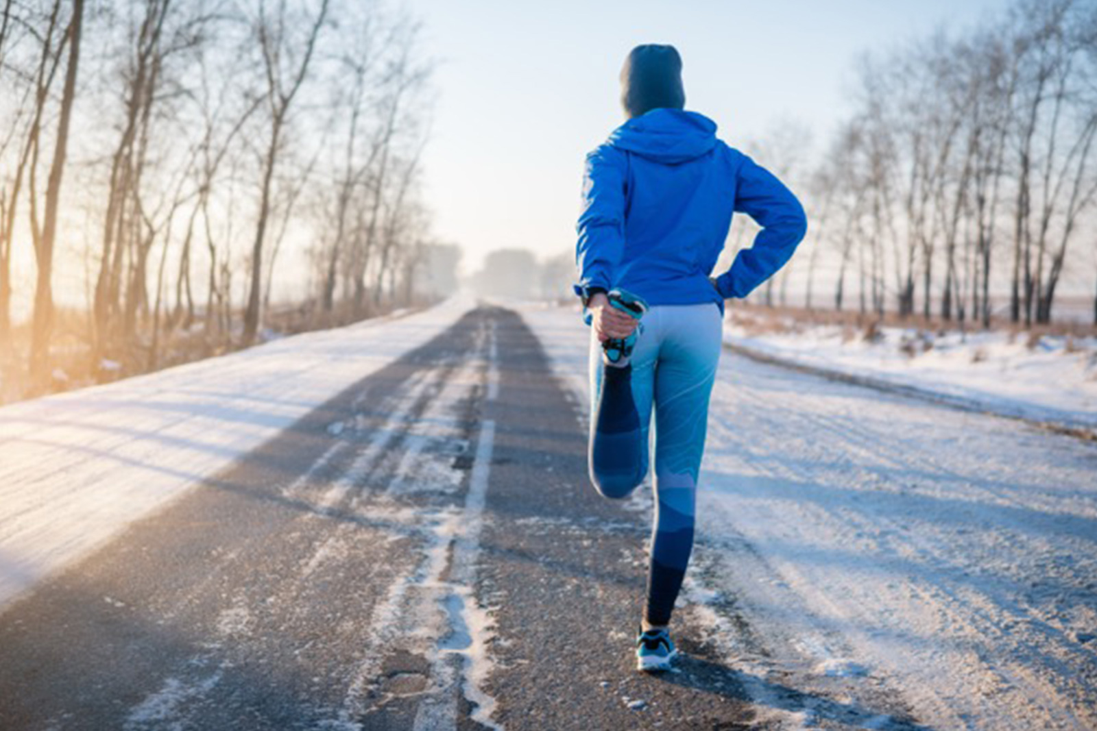 A woman wearing running attire navigates a snowy road in winter, highlighting her commitment to fitness despite the elements.