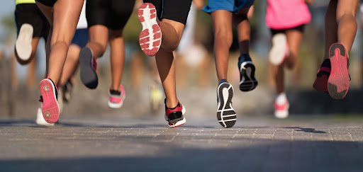 Low-angle shot of a large group of runners' feet mid-stride on a paved road during a race.