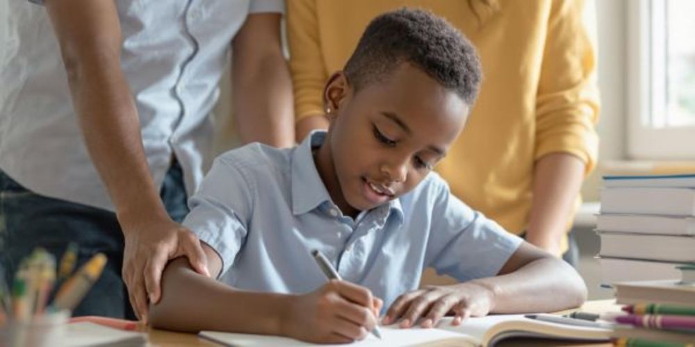 child-writing-with-parents-standing-behind-him.jpg