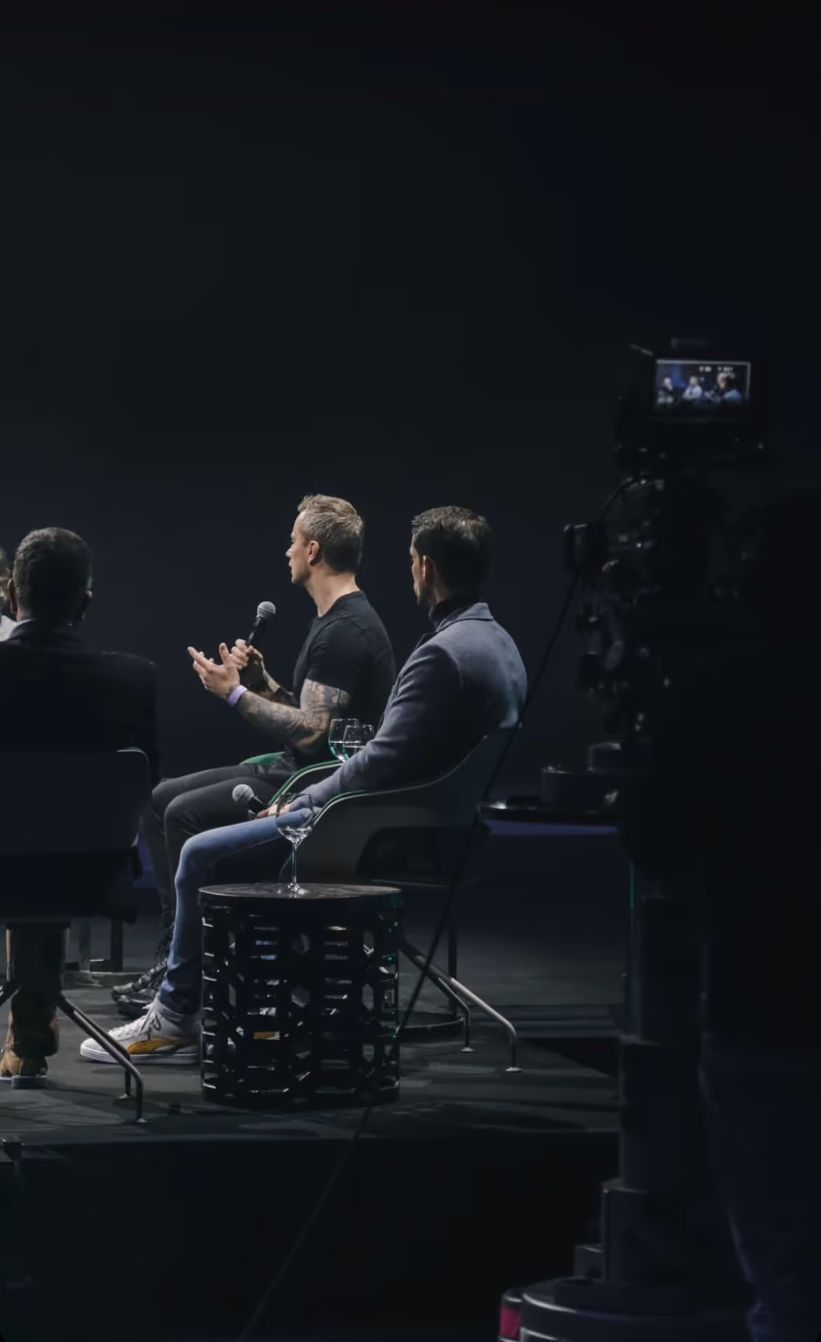 Three men sitting on stage discussing with microphones during a panel event.