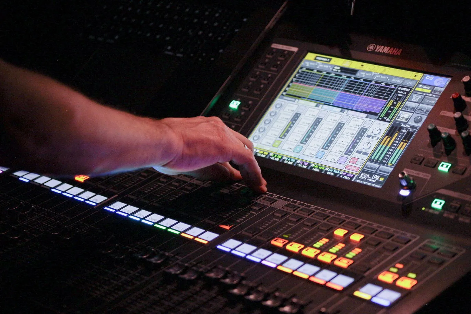 A person adjusts controls on a digital audio mixing console with a colorful display screen.