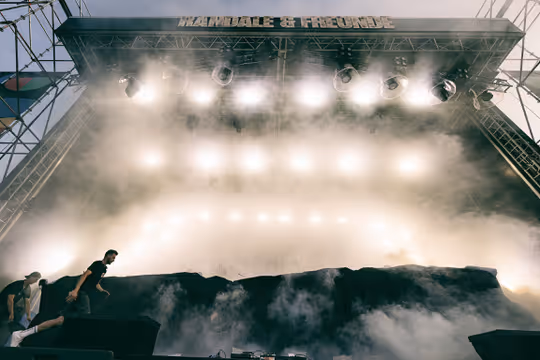 A stage with bright lights and fog is being set up by workers.