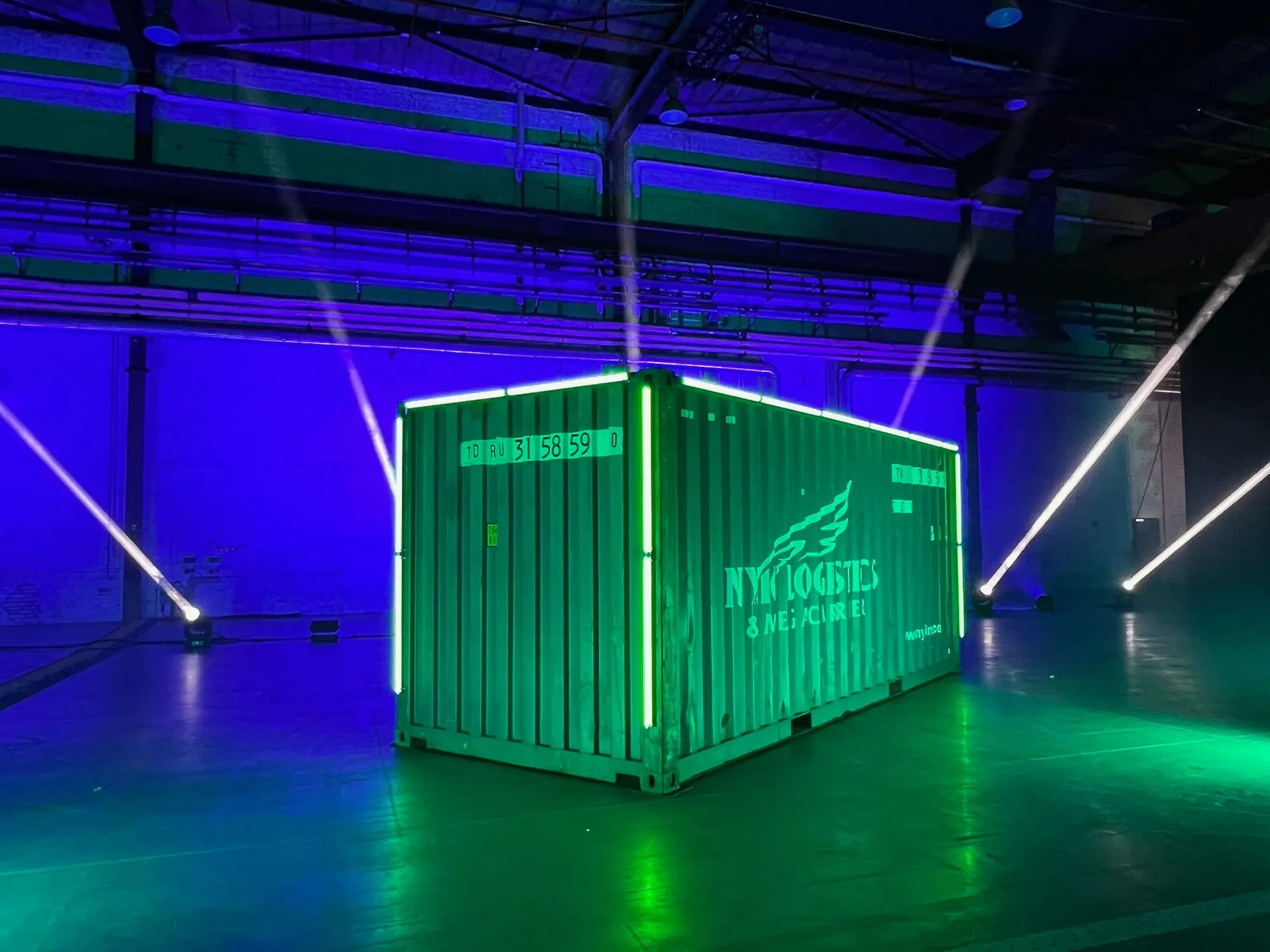 A shipping container is illuminated with green lights inside a dark warehouse.
