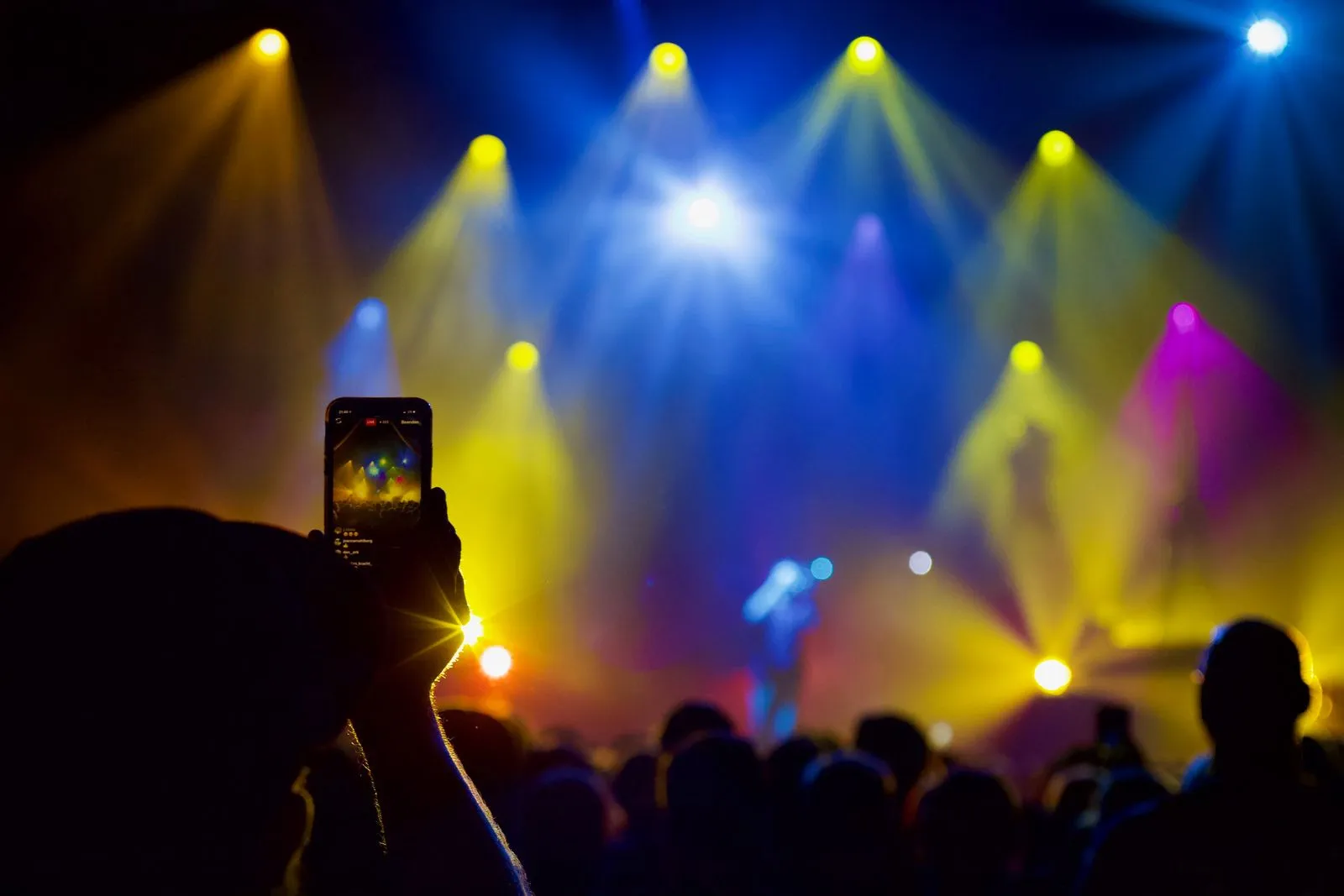 Eine Person hält sein Handy hoch und filmt ein sehr farbenfrohes Live Konzert
