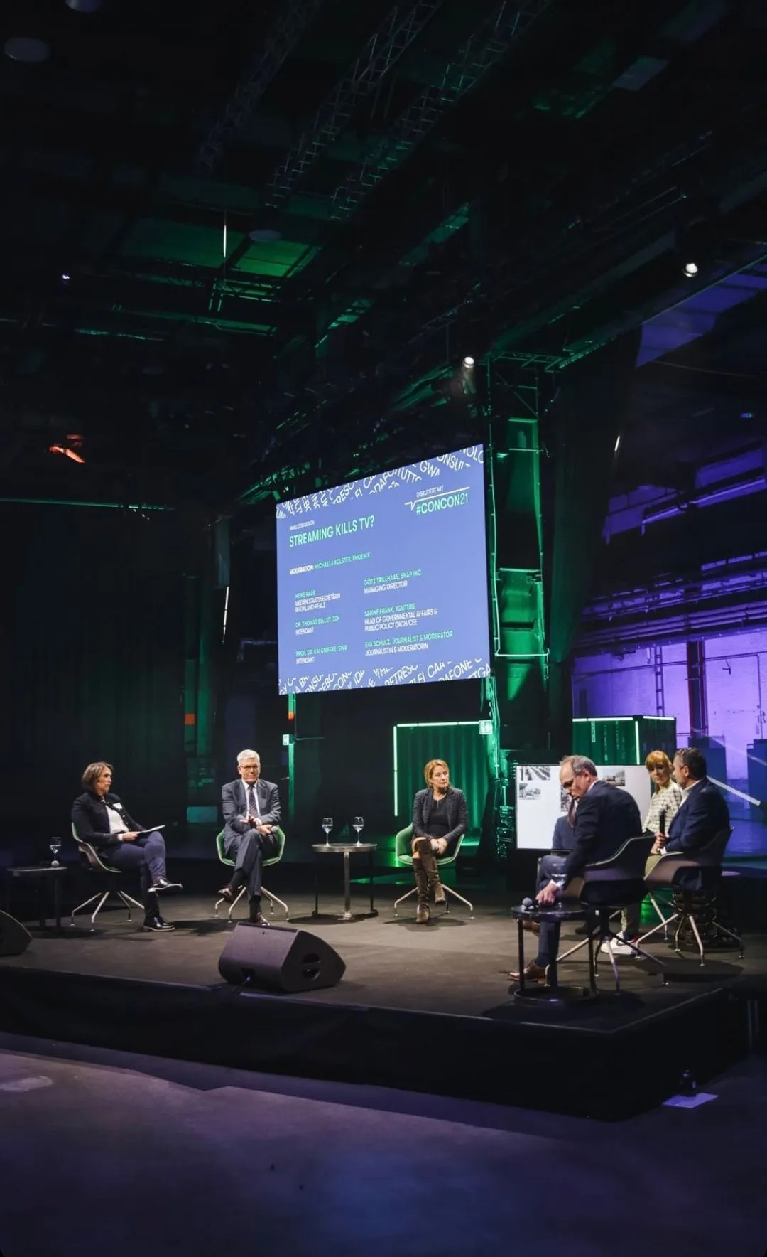 Sechs Menschen sitzen in einer Panel Diskussion unter einer LED Leinwand, die die Panel Diskussion begleitet
