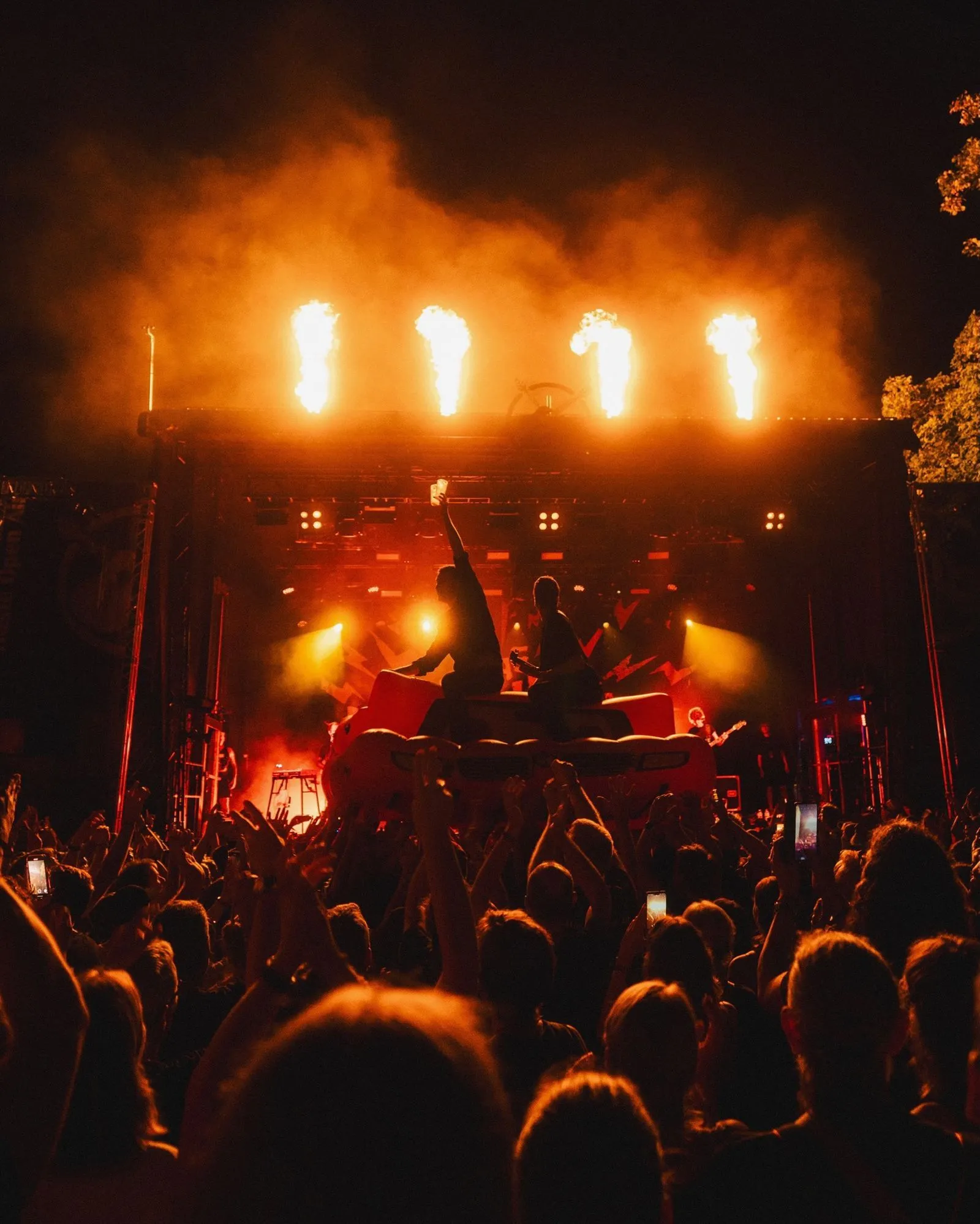 Crowd cheering at a concert with performers on stage and flames shooting from above.