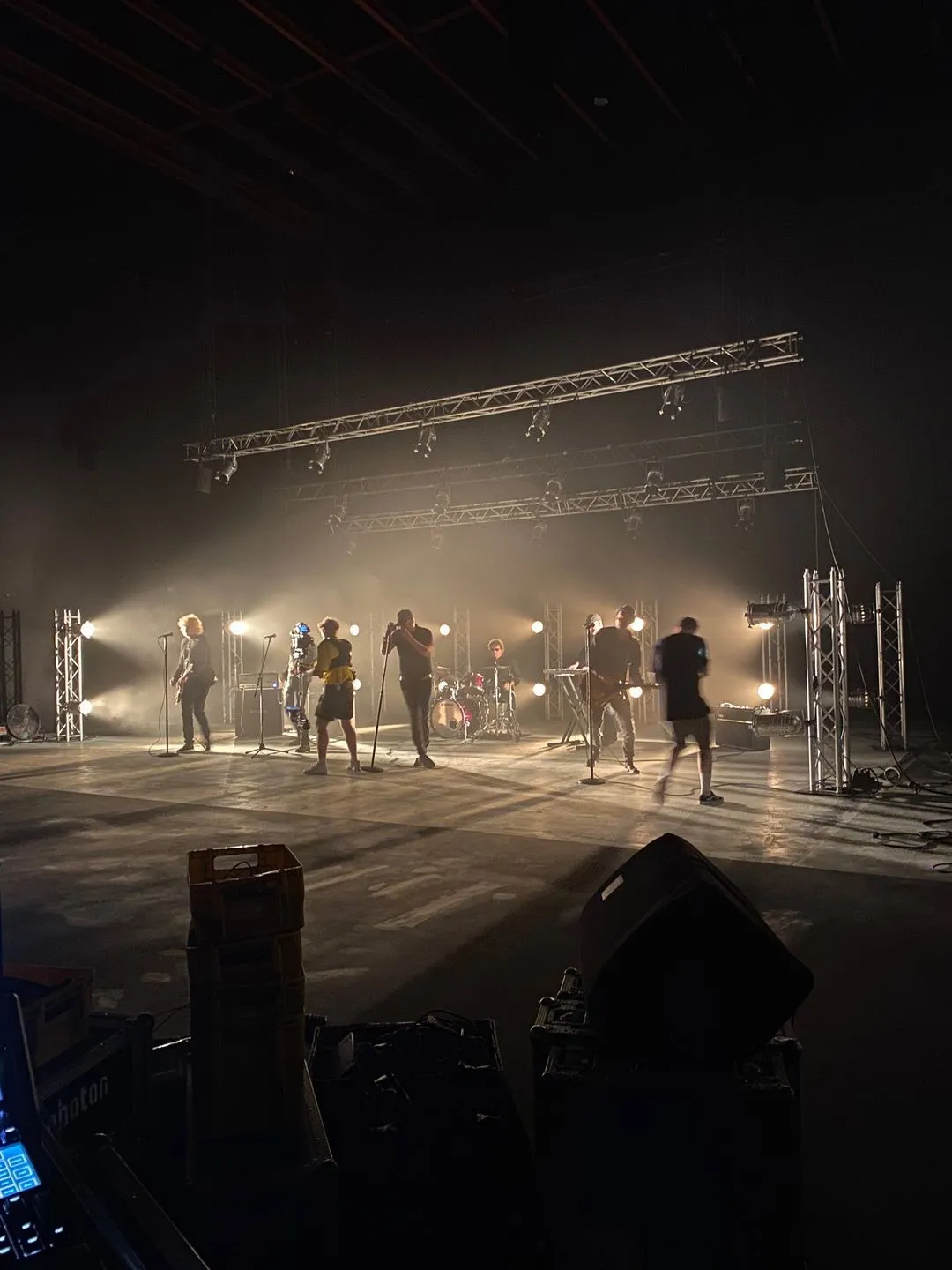 A band rehearses on stage with bright spotlights shining around them.