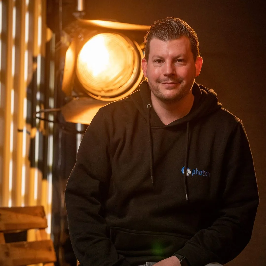 Man in a hoodie sitting indoors with a bright spotlight behind him.