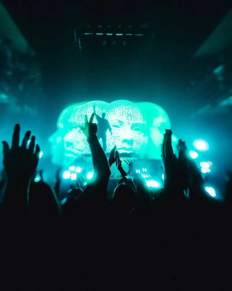 Eine Große Gruppe von leuten schaut einem DJ bei seiner Show zu. Im hintergrund ist eine LED wand zu sehen die drei Köpfe Zeigt in weiss.