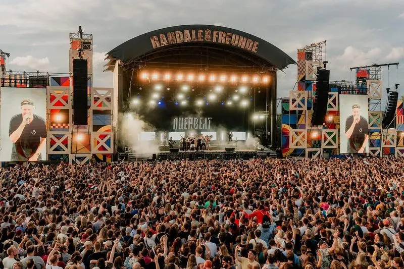 Eine große Menschenmenge steht vor einer Bühne, auf der die Band querbeet performt über der Bühne steht. Randale und Freunde sind etwa 30.000 Menschen, die der Band zu jubeln.