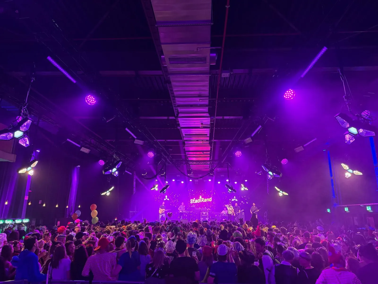 eine Große halle voll mit menschen auf einer Tanveranstaltung mit viel Lichttechnik unter der Decke