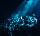 Eine Gruppe von Musikern steht in einer Rehei und wird von Hinten mit Movinglights angeleuchet