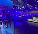 Ein Blau illuminierter Raum. vorne Links im Bild findet sich ein Glaskasten von dem aus ein Gamer seinen Livestream streamt und dahinter ein Großes Fernsehstudio welches blau ausgeleuchtet ist.