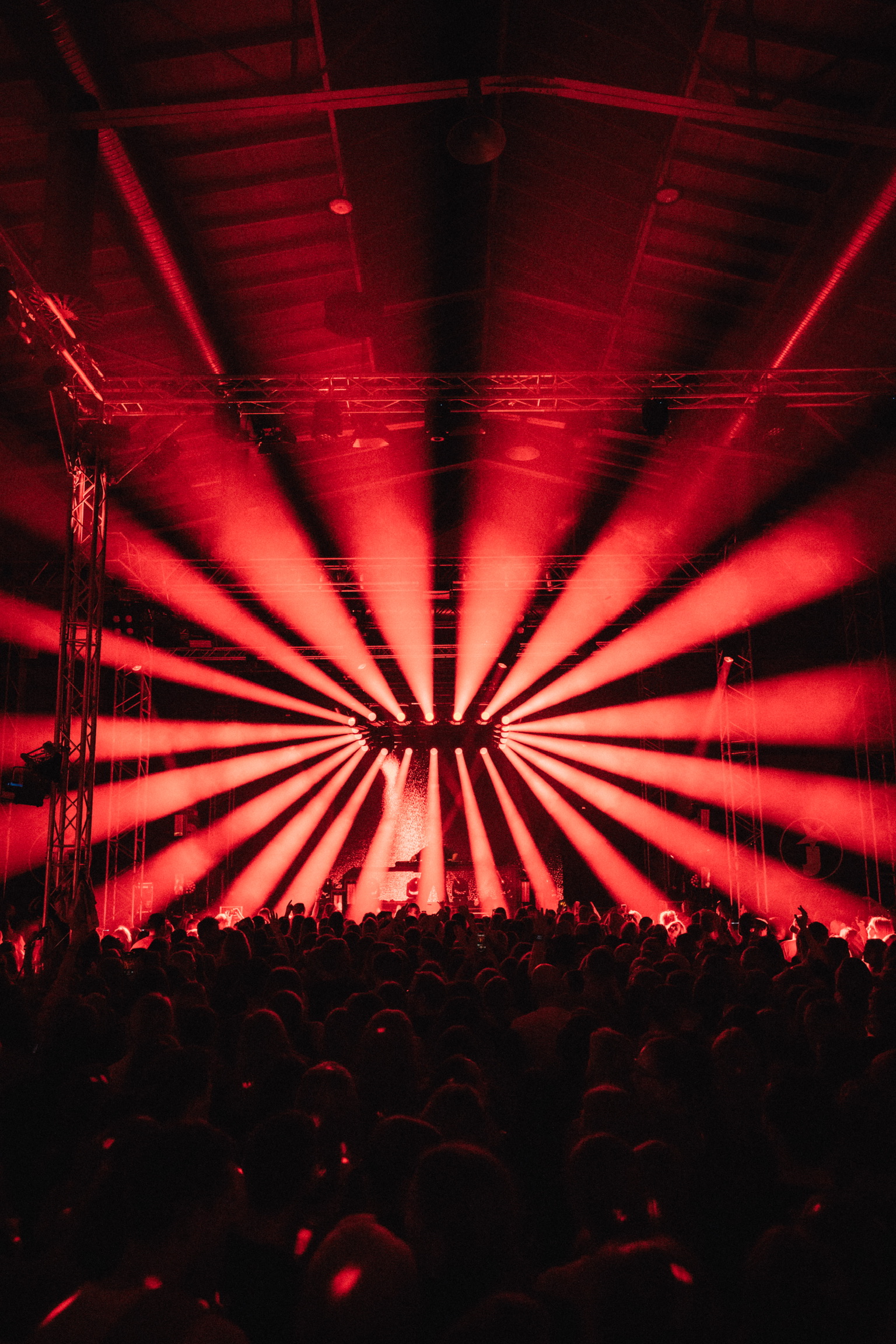 Eine Menschenmenge steht vor einer Bühne auf der ein DJ untermalt mit Lichttechnik, performt. Die Lichtstrahlen sind orange