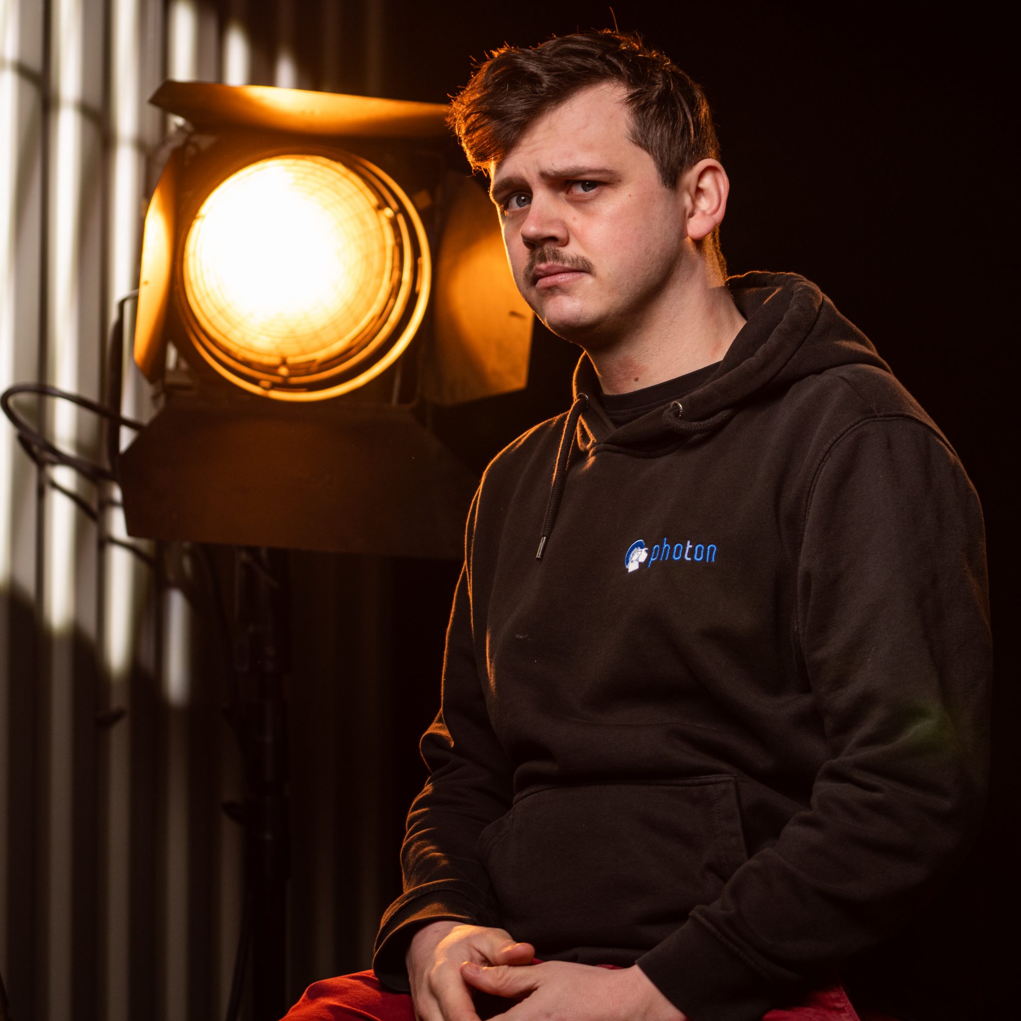 Jonathan Dornando mit dunklen Haaren und einem Schwarzen Hoody lächelt in die Kamera, eine Stufenlinse steht hinter ihm