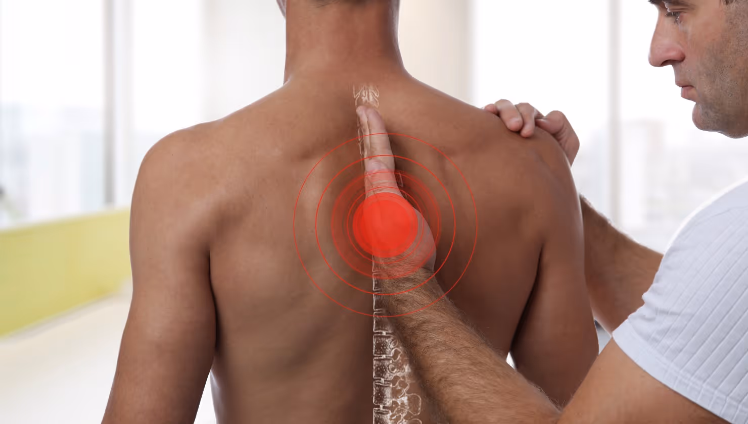 Therapist examining a man's back with a red target highlighting mid-spine pain area and a spine illustration overlay.