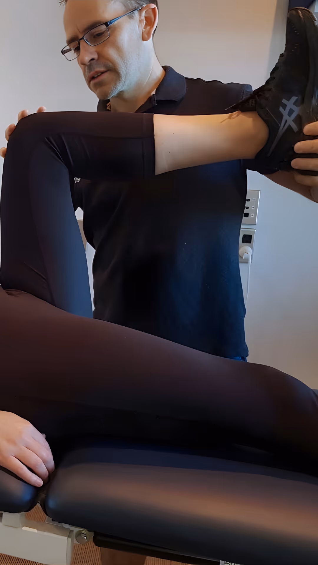 A physiotherapis at Vigeo Physio (Dominic Brosnahan) stretching a patient's bent leg on a treatment table.