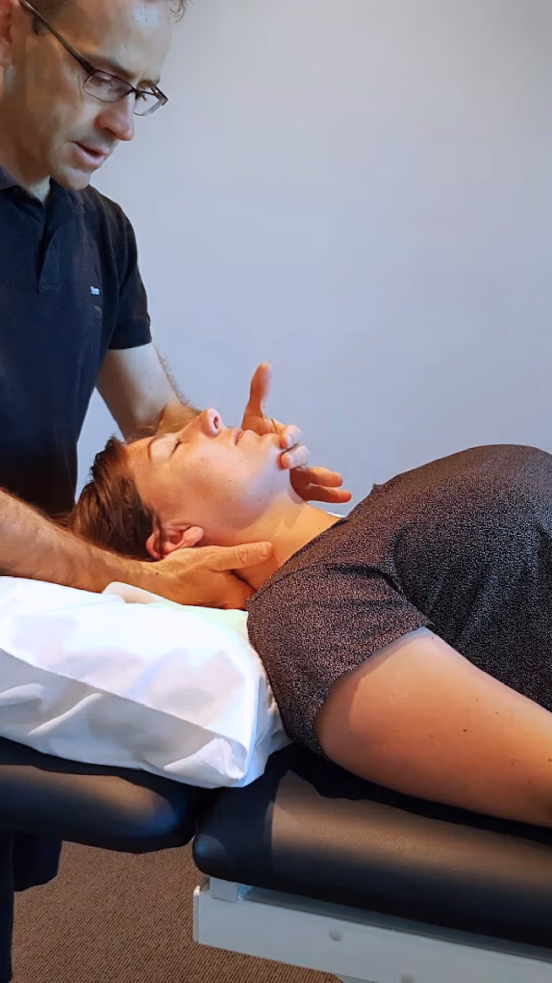 Physical therapist assisting a woman in black leggings with a leg stretch on a treatment table.