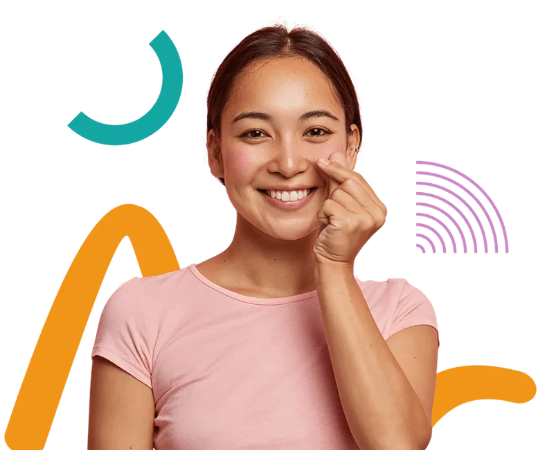 Smiling woman in a light pink shirt making a finger heart gesture, a popular symbol of affection, with colorful abstract shapes in the background. Her cheerful expression and casual pose convey warmth and friendliness.
