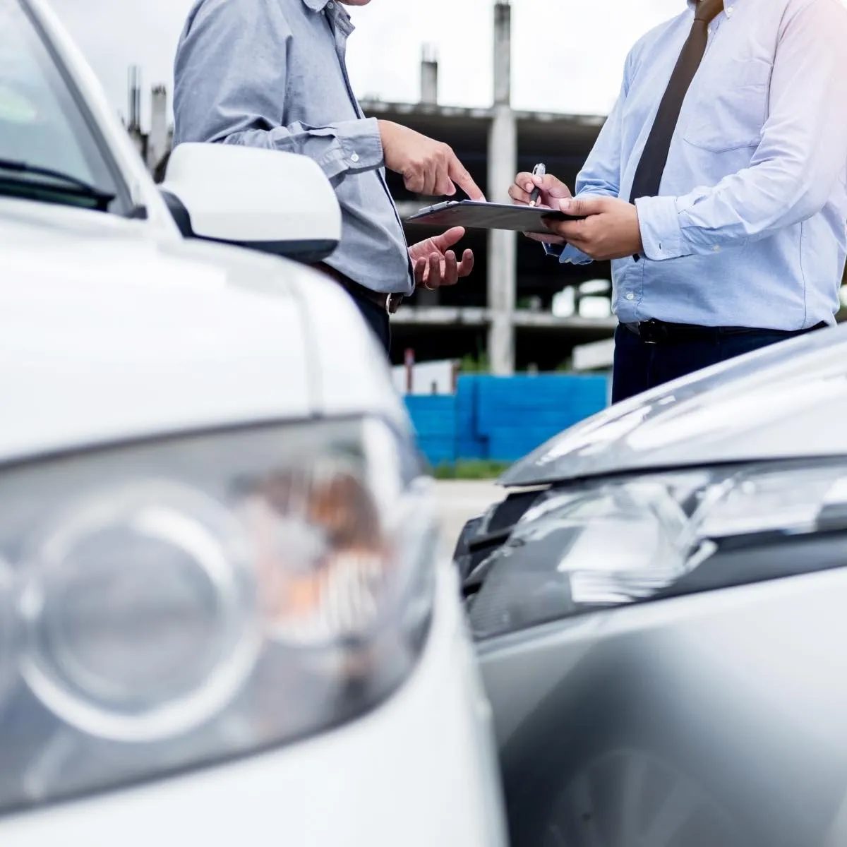 Two men discussing and reviewing a clipboard near two cars involved in a minor accident.
