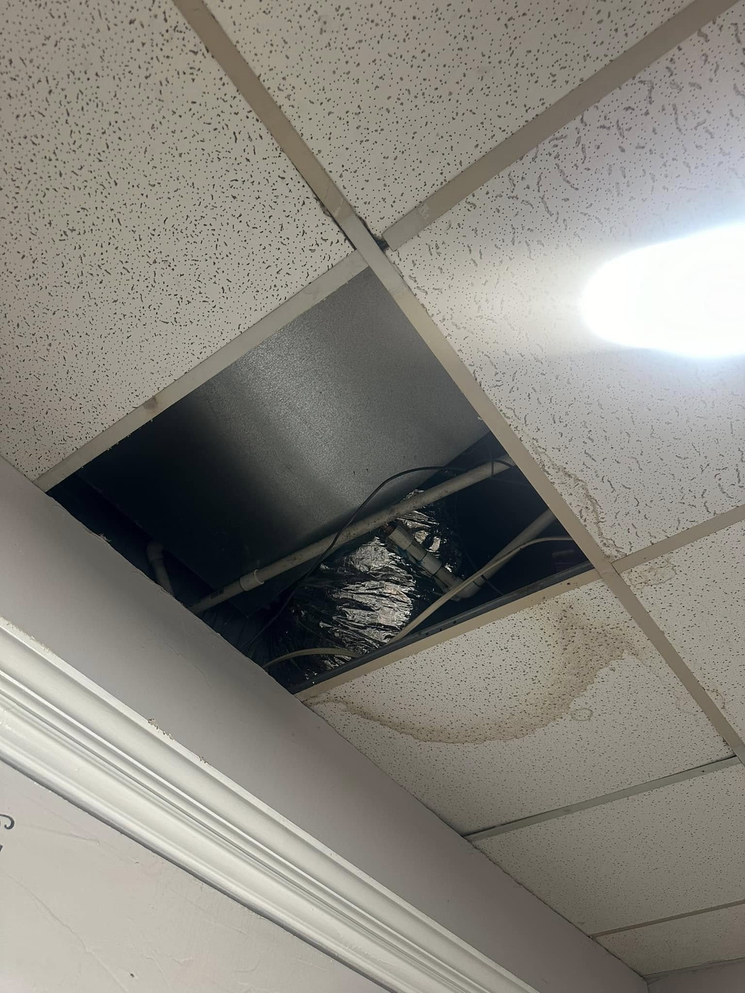 Ceiling tiles removed showing leaking pipes and water damage.