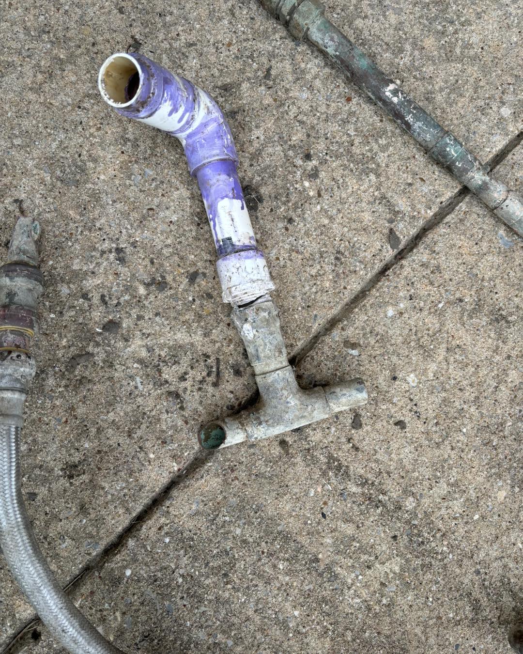 Old corroded pipe fitting and PVC pieces laid on concrete.