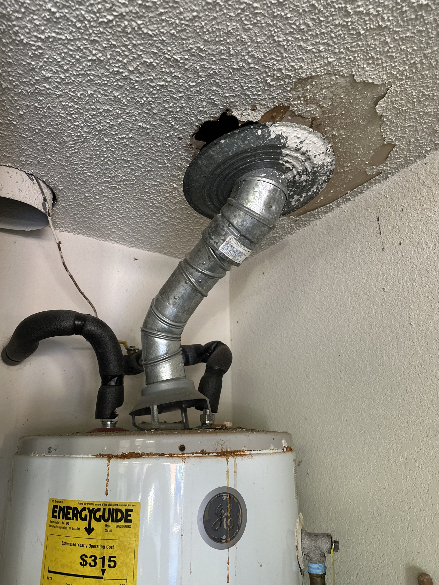 Damaged ceiling above a water heater with vent pipe corrosion.