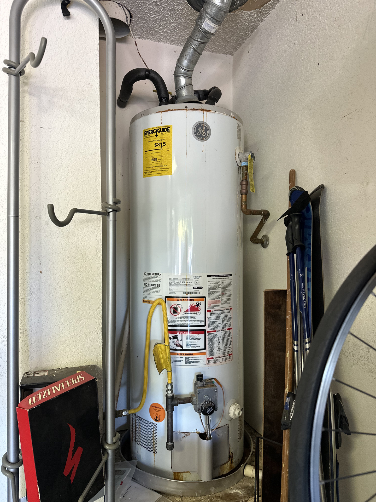 Old water heater with rust and vent damage in a garage.