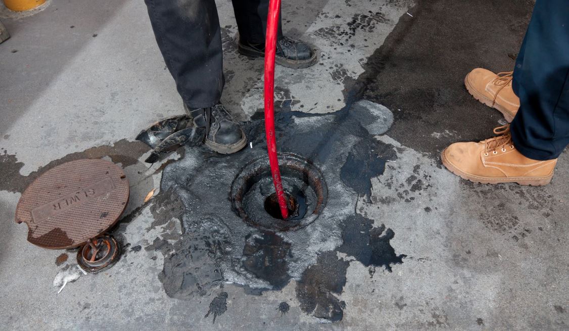 Hydrojet hose inserted into a sewer cleanout on a dirty floor.