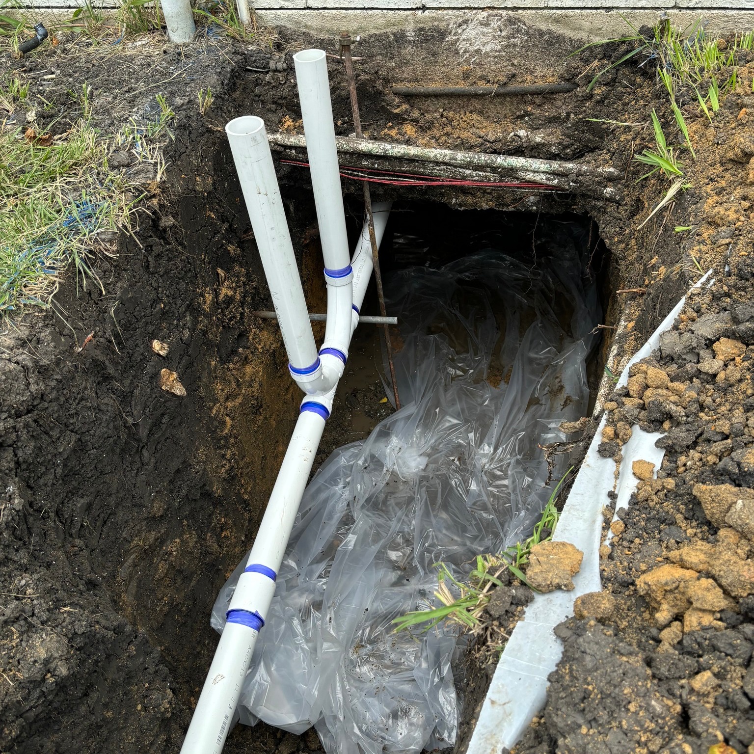 PVC drain pipes installed in a trench during underground plumbing work.