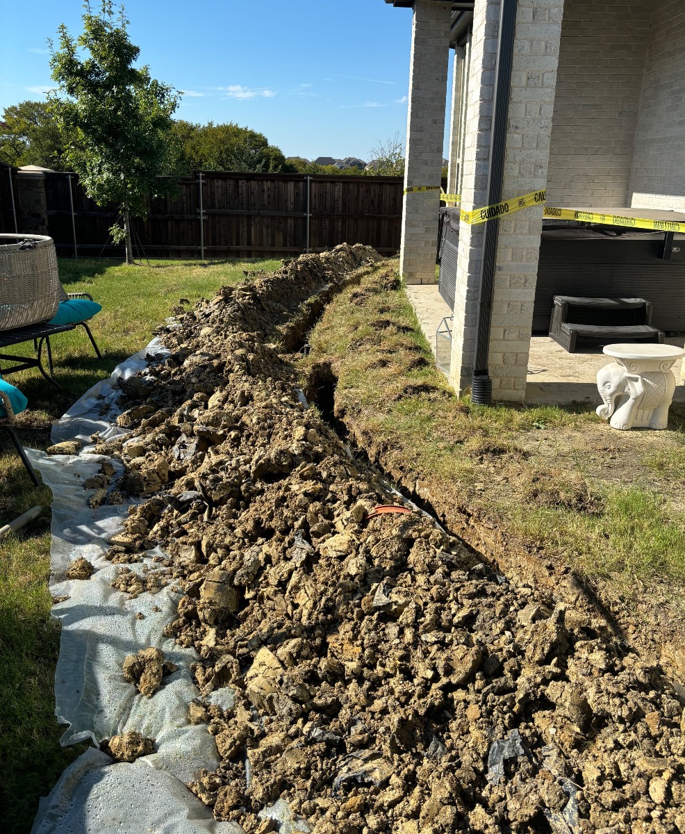 Freshly dug trench along a backyard for water line repair.