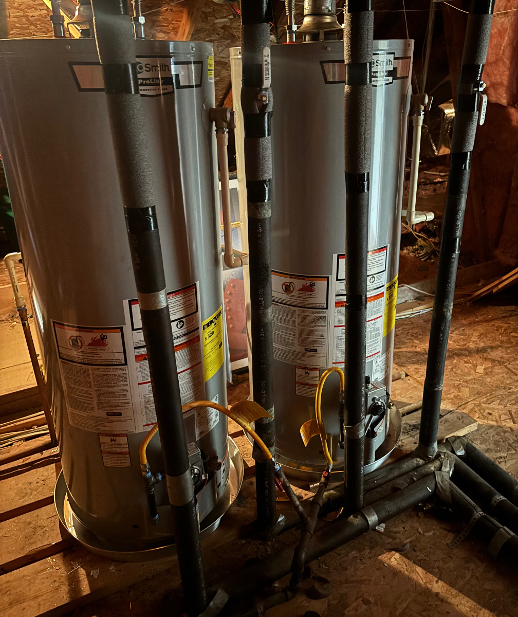 Two water heaters installed side by side in an attic.