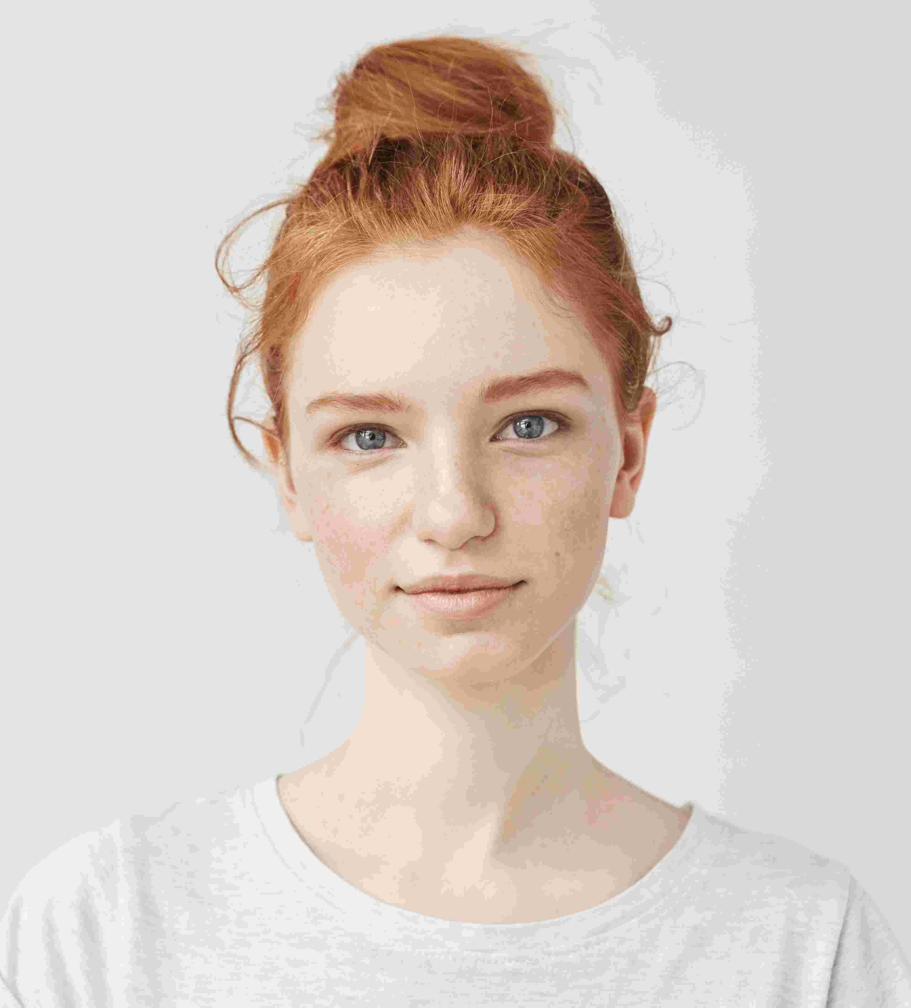 Portrait of a young woman with red hair in a bun, blue eyes, and light skin wearing a white shirt.