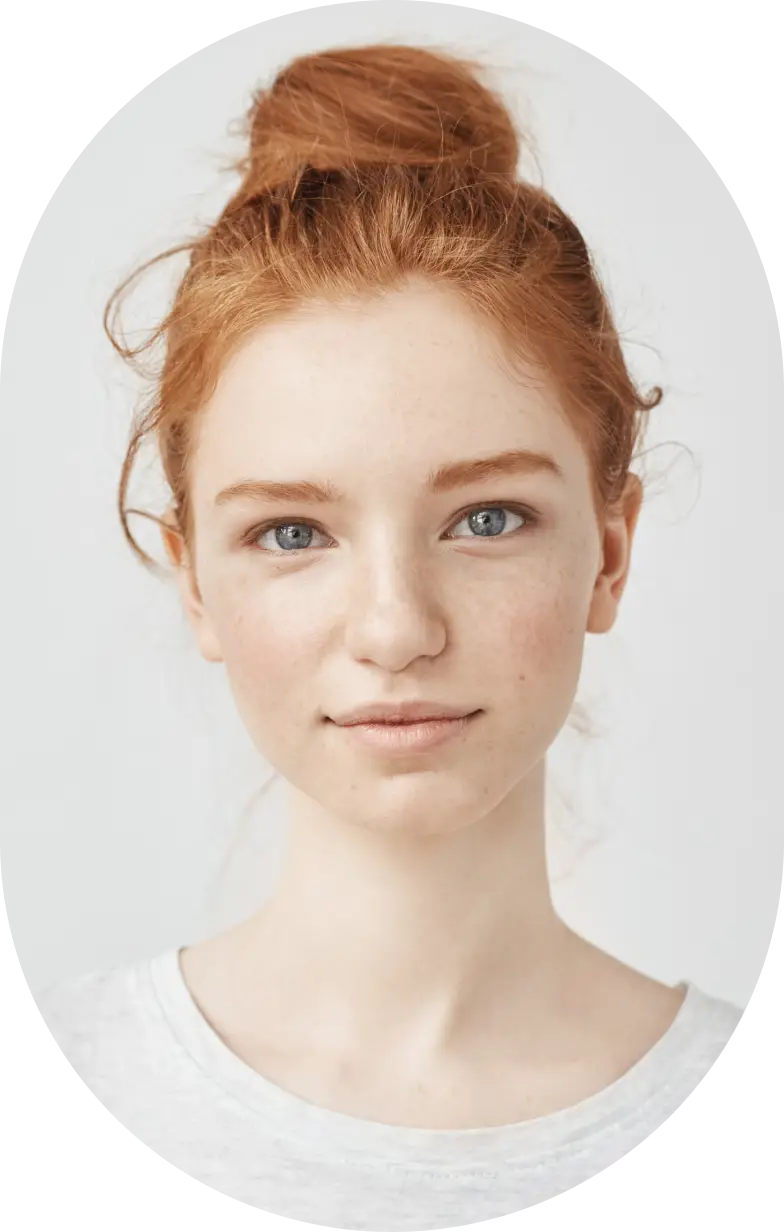 Portrait of a young woman with red hair tied in a bun, blue eyes, light skin, and a neutral expression wearing a white shirt.