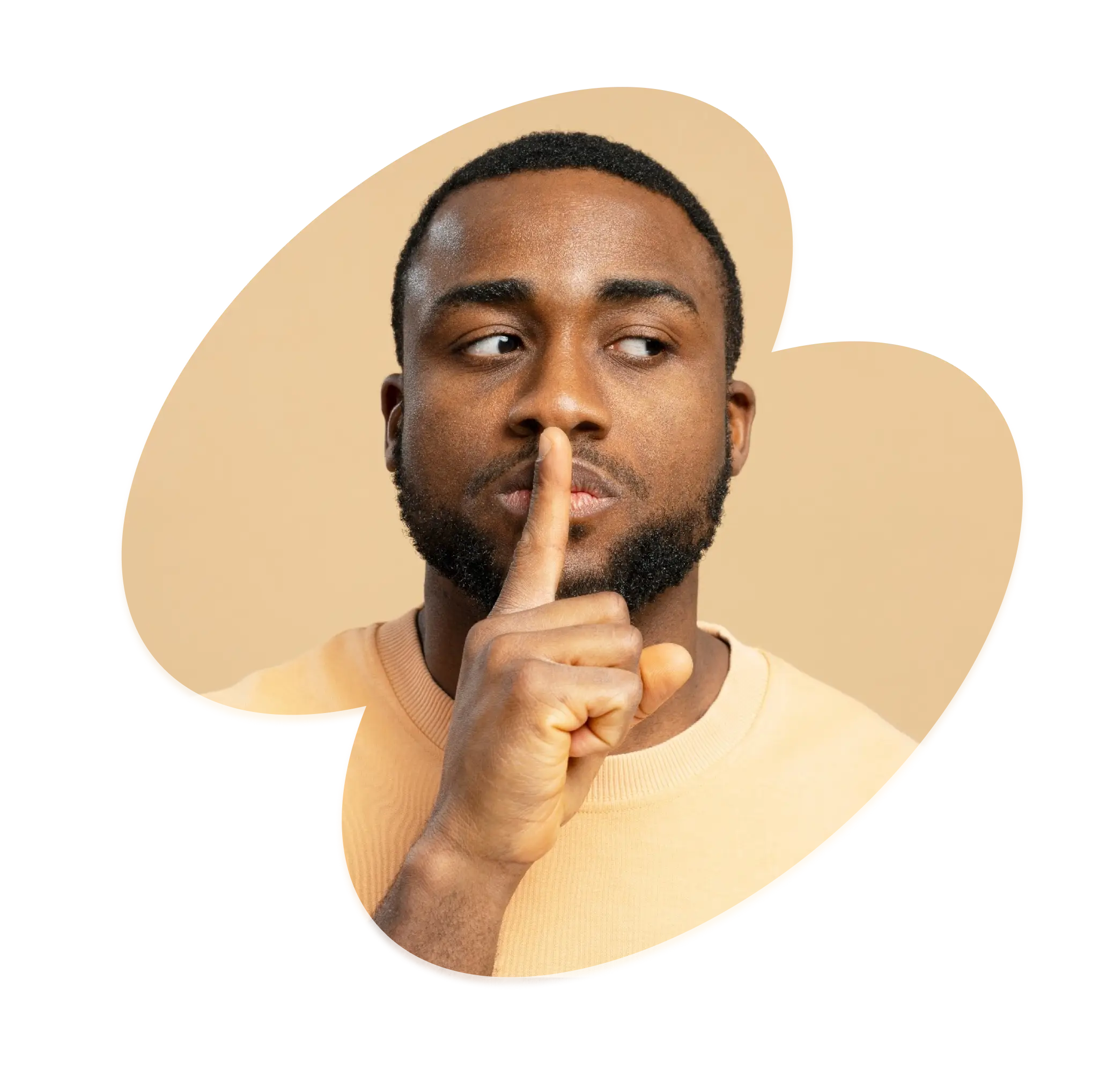 Man with a beard wearing a beige sweater holding a finger to his lips in a shushing gesture.