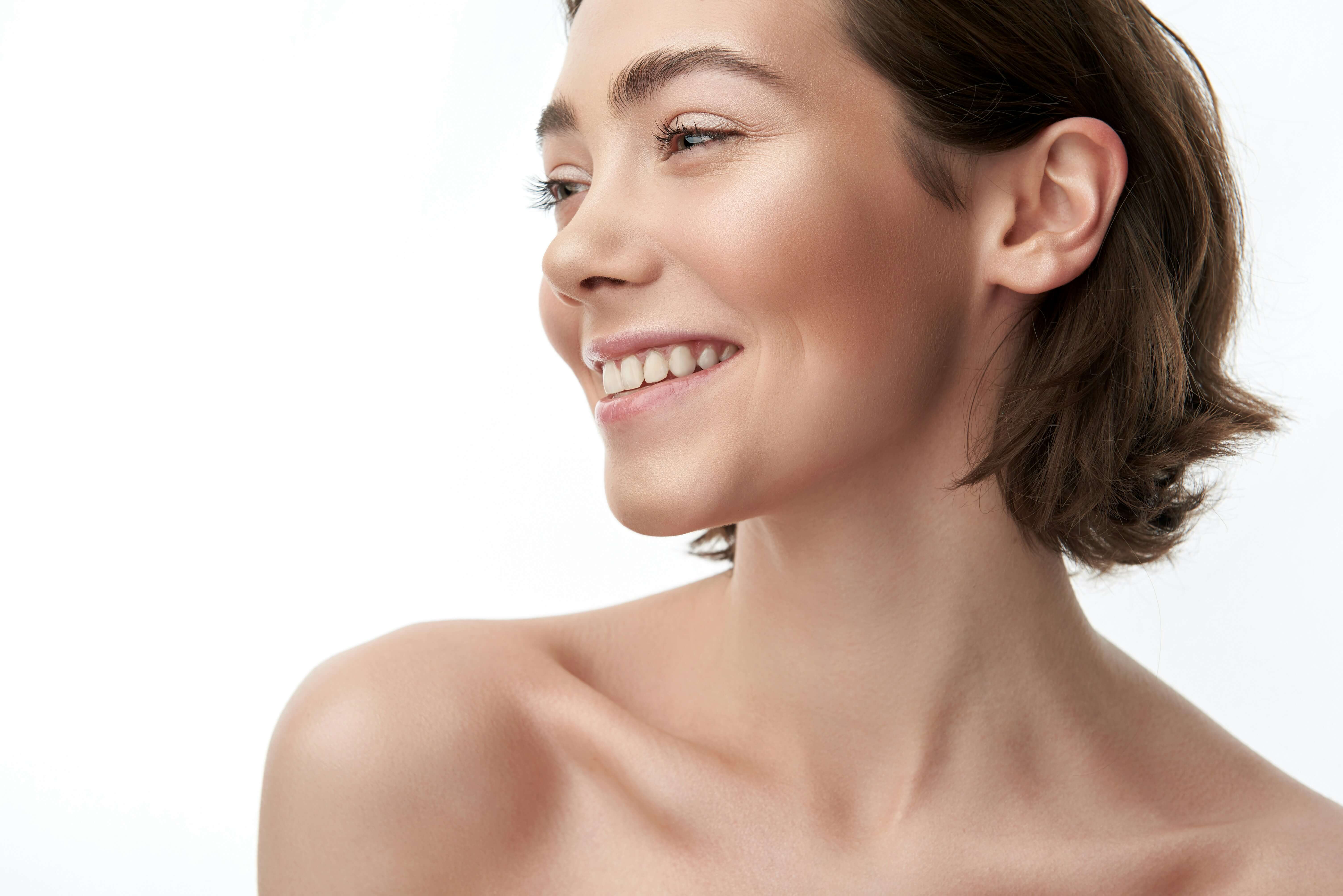 Close-up profile of a smiling woman with short brown hair and bare shoulders against a white background.